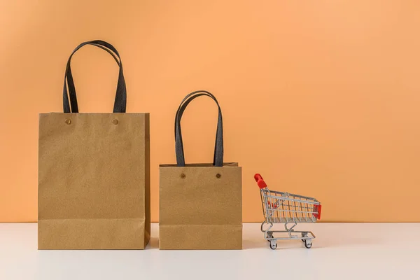 Papieren boodschappentassen en winkelwagen of trolley op witte tafel — Stockfoto