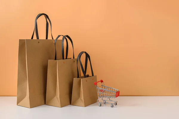 Bolsas de compras de papel y carrito de compras o carro sobre mesa blanca —  Fotos de Stock