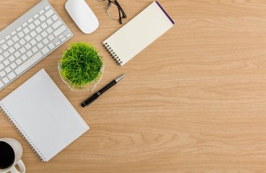 Üst Manzara Ahşap ofis masası. Ağaç tenceresi, klavye, fare bilgisayarı, defter, kahve fincanı, gözlük, ahşap arka planda kalem ofis malzemeleri olan düz bir çalışma alanı
