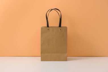 Beyaz masa ve pastel turuncu arka planda kahverengi kağıt alışveriş torbası. İleti ve logonuz için kopyalama alanı ile
