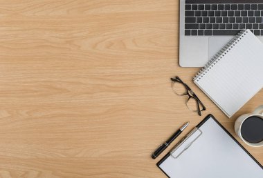 Üst Manzara Ahşap ofis masası. Göz gözlüğü, dizüstü bilgisayar, not defteri, not panosu, kalem, ahşap arka planda kahve fincanı ofis malzemeleri olan düz bir çalışma alanı.