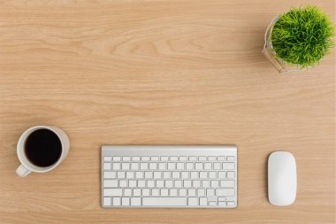 Üst Manzara Ahşap ofis masası. Ağaç tenceresi, klavye, fare bilgisayarı, kahve fincanı ofis malzemeleriyle ahşap masa arkasında düz bir çalışma alanı.