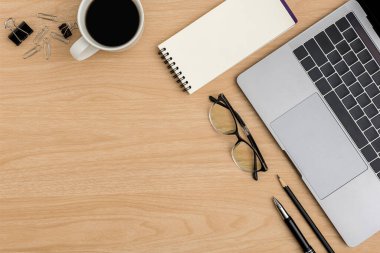 Üst Manzara Ahşap ofis masası. Göz gözlüğü, kahve fincanı, dizüstü bilgisayar, ataç, not defteri, ahşap arka planda kalem ofis malzemeleri ile düz yerde yatıyordu.