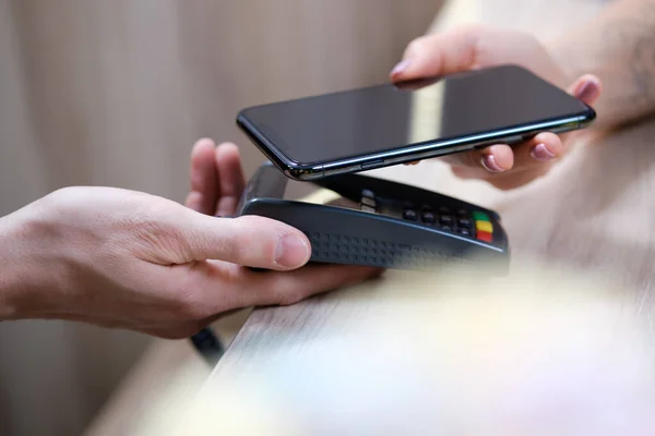 Close up of female client hold smartphone paying for order using modern easy nfc technology, waiter give card reader machine for customer make payment transaction with cashless contactless metho