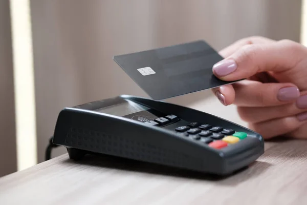 Müşteri eli NFC teknolojisiyle bağlantısız kredi kartıyla ödeme yapıyor. Barda kredi kartı okuma makinesi olan bir barmen ve elinde kredi kartı olan bir kadın. Ellere odaklan.