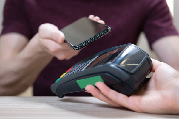 Крупным планом мужчины клиент держать смартфон платить за заказ с помощью современной простой технологии NFC, официант дать кард-ридер машину для клиента совершать платежные операции с безналичным бесконтактным методом
