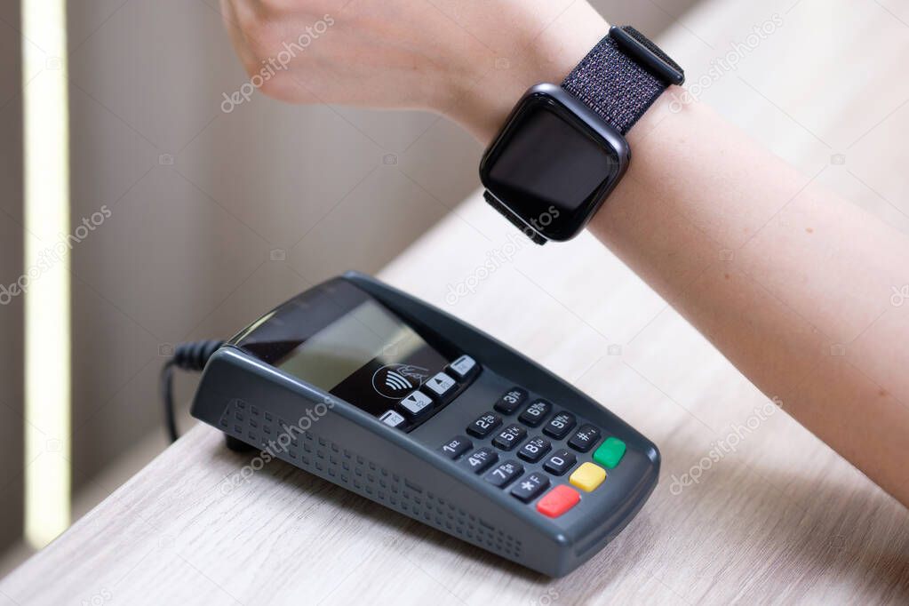 Woman using terminal for contactless payment with smart watch indoor