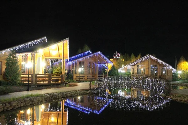 Casa de madera por la noche. El pueblo está decorado con hermosas luces. Iluminaciones. Noche de primavera en el pueblo . —  Fotos de Stock