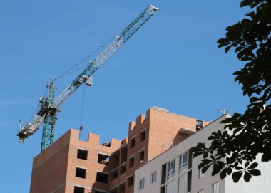 Mavi gökyüzüne karşı inşaat halindeki vinç ve bina.