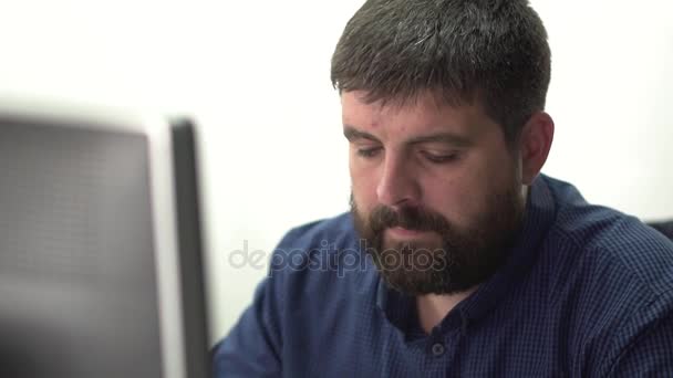 Den ansatte på kontoret jobber foran dataskjermen. Han snakker i telefonen i hodetelefonene. . – stockvideo