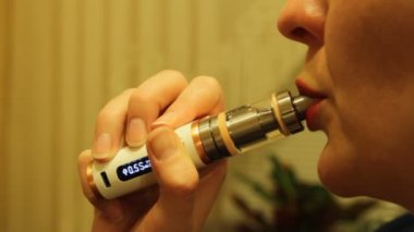 Kız bir elektronik sigara Buharlaştırıcı içiyor ve onun ağzından duman buharı bültenleri.