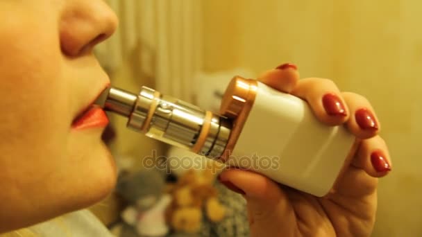 La ragazza fuma un vaporizzatore elettronico di sigarette e rilascia vapore di fumo dalla bocca . — Video Stock