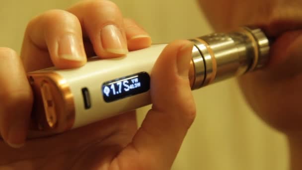 Dziewczyna pali odparowalnik elektroniczny papieros i zwalnia dym pary z jej ust. — Wideo stockowe