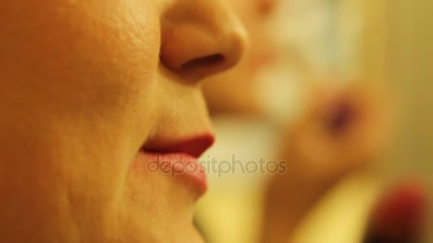 Молодая красивая блондинка красит губы ярко-красной помадой перед зеркалом — стоковое видео