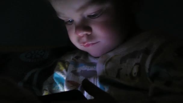 Pojke på två år titta på tecknade serier på sin surfplatta på natten — Stockvideo