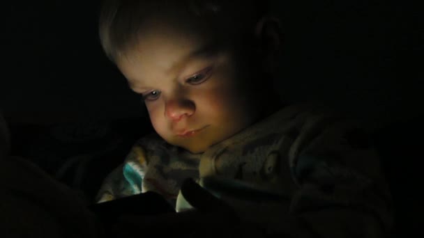 Мальчик двух лет смотрит мультфильмы на своем планшете по ночам — стоковое видео