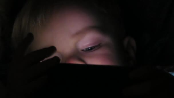 Хлопчик два роки дивиться мультфільми на планшеті вночі — стокове відео