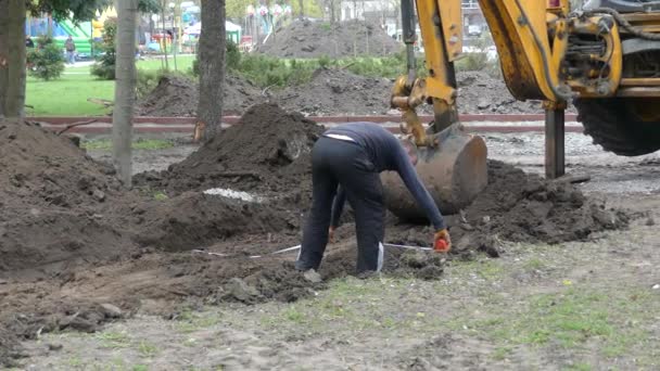 2018年4月19日 乌克兰 挖掘机的水桶挖地面 工人用建筑测量胶带测量沟槽 — 图库视频影像