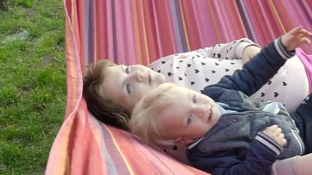 日落时 孩子们在城市公园的一个彩色吊床上休息 一个男孩和一个女孩在公园的吊床上休息 — 图库视频影像