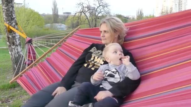 母と息子は 日没時に都市公園における色のハンモックで休みます 少年と彼の母親が公園でハンモックで休む — ストック動画
