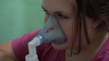 Genç kız oksijen maskesini içine çekiyor. Solunum yolu solunumu. Maske astım spreyi.