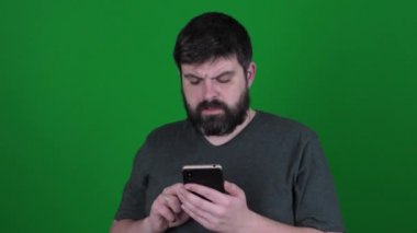 Bearded man communicates on Skype on a green background. A bearded man is talking via video link on a green chroma key. A man screams into a smartphone.