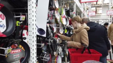 Europe, Kiev, Ukraine, - February 2020: A woman chooses a frying pan in the market. Pans on a shelf in a store. Cookware.