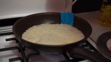 Europe, Kiev, Ukraine - March 2020: a girl bakes pancakes in a pan. Pan with pancake on a gas stove.