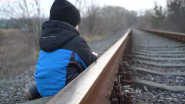 4歳の少年が線路で遊んでいる 黄色い道の子供がレールで遊んでいる 鉄道の危険性 — ストック動画