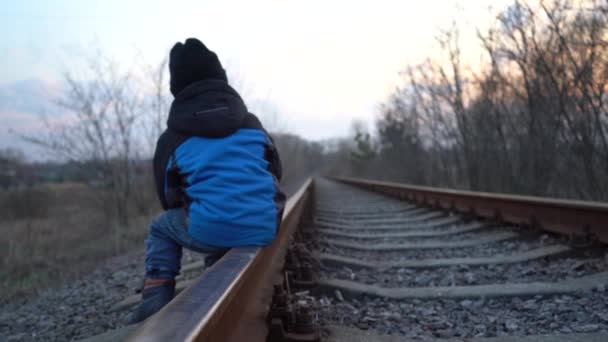 4歳の少年が線路で遊んでいる 黄色い道の子供がレールで遊んでいる 鉄道の危険性 — ストック動画