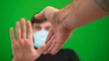 Maskeli sakallı bir adam ellerini antiseptik ve şakalarla kirletiyor. Yeşil bir arka planda. Covid-19 koronavirüs salgınında hoş geldin işareti. Dur, elini göster. El sıkışalım. Toplantıda selamlar. Virüsün yayılması.