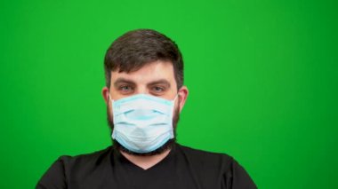 Maskeli sakallı bir adam ellerini antiseptik ve şakalarla kirletiyor. Yeşil bir arka planda. Covid-19 koronavirüs salgınında hoş geldin işareti. Dur, elini göster. El sıkışalım. Toplantıda selamlar. Virüsün yayılması.