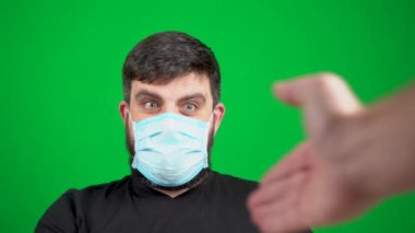 Maskeli sakallı bir adam ellerini antiseptik ve şakalarla kirletiyor. Yeşil bir arka planda. Covid-19 koronavirüs salgınında hoş geldin işareti. Dur, elini göster. El sıkışalım. Toplantıda selamlar. Virüsün yayılması.