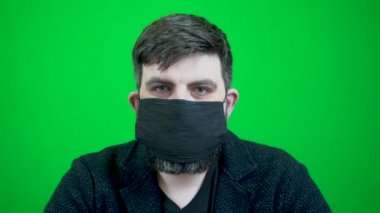 Sakallı bir adam koronavirüs salgını sırasında birçok tıbbi maske takar. Birçok tıbbi maske sakallı bir adama takılır. Bir adamın üzerinde bir kaç tane sargı bezi var. Yeşil arka planda bir yüzün yakın plan görüntüsü.