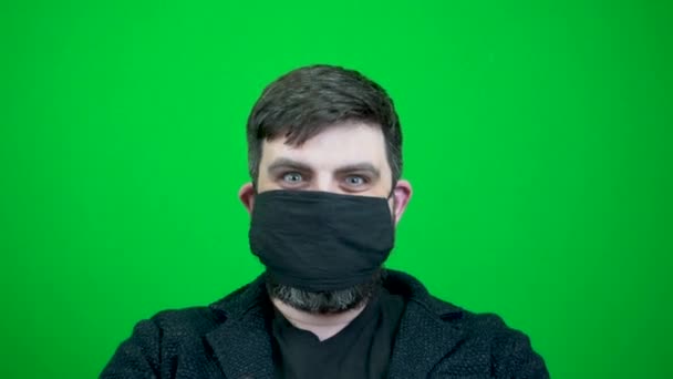一个留着胡子的男人在一场大脑皮层病毒大流行时戴上了许多口罩 很多口罩都戴在一个留着胡子的男人身上 男人身上穿的几件医装 在绿色背景上的面部特写 — 图库视频影像