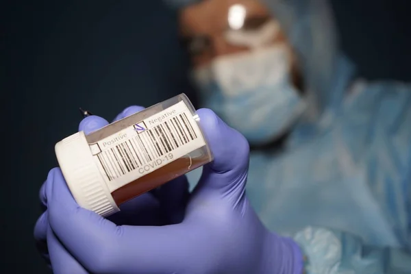 A doctor in a protective medical suit holds a flask with samples of Covid-19. The result of the \