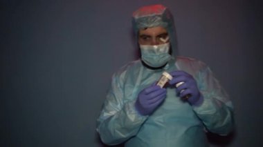 Koruyucu giysili sakallı bir doktor Covid-19 Coronavirus salgını sırasında laboratuvar şişelerini analiz için kontrol ediyor. Sisli maskeli yorgun doktor.