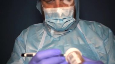 Koruyucu giysili sakallı bir doktor Covid-19 Coronavirus salgını sırasında laboratuvar şişelerini analiz için kontrol ediyor. Sisli maskeli yorgun doktor.