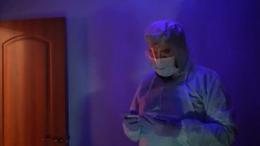 Laboratuvarda anksiyete sırasında koruyucu giysi giymiş sakallı bir doktor. Coronavirus salgını sırasında laboratuvarda bir kaza olmuş. Sirenin ışığı mavi-kırmızıdır. Odadaki kötü ışığın etkisi..