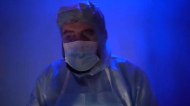 Laboratuvarda anksiyete sırasında koruyucu giysi giymiş sakallı bir doktor. Coronavirus salgını sırasında laboratuvarda bir kaza olmuş. Sirenin ışığı mavi-kırmızıdır. Odadaki kötü ışığın etkisi..