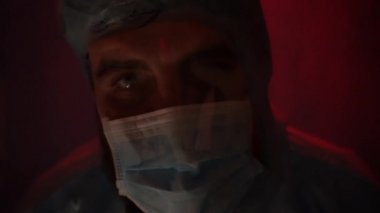 Laboratuvarda anksiyete sırasında koruyucu giysi giymiş sakallı bir doktor. Coronavirus salgını sırasında laboratuvarda bir kaza olmuş. Sirenin ışığı mavi-kırmızıdır. Odadaki kötü ışığın etkisi..