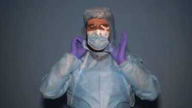 Yorgun bir doktor koronavirüs salgını sırasında koruyucu giysisini çıkarır. Terli bir doktor vardiyanın sonunda tıbbi bir maske ve eldiven çıkarıyor..