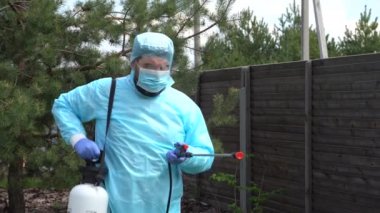 Koruyucu kabuklu biri özel bir kulübede Covid-19 'a karşı önlem olarak dezenfektan sıkar. Salgın ölçümleri. Virüse karşı antiseptik temizlik. Pine, böcek ilacı püskürtüyor. Kameraya serpiliyor..