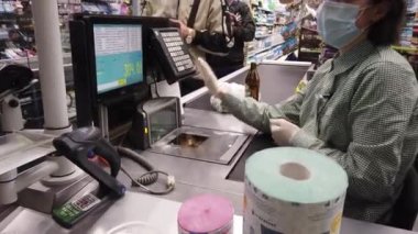 Avrupa, Kiev, Ukrayna - Nisan 2020: Covid-19 Coronavirus salgını sırasında bir süpermarkette tıbbi maske takan bir alıcı yiyecek parasını ödüyor. Süpermarkette nakit masası. Tuvalet kağıdı.