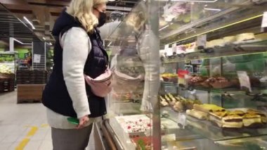 Avrupa, Kiev, Ukrayna - Mayıs 2020: Maskeli bir alıcı süpermarkette şeker seçiyor. Pastalar markette.