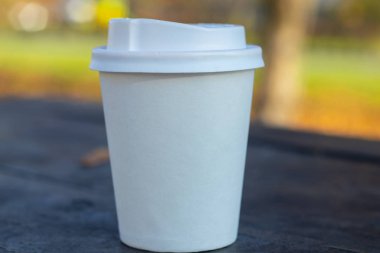 Tahta bir masanın üzerinde kahve kapağı ve kuru sarı akçaağaç yaprakları olan beyaz kağıt bardak.