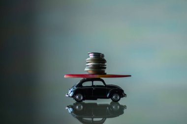 Üzerinde sörf tahtası olan küçük bir oyuncak araba ve aynada duran küçük bir para yığını.