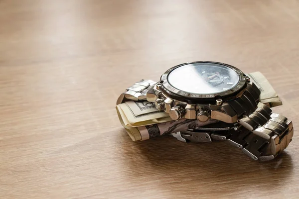 dollars invested in men\'s watches lie on a table in the sunlight