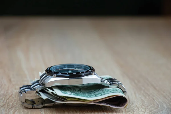 dollars invested in men's watches lie on a table in the sunlight