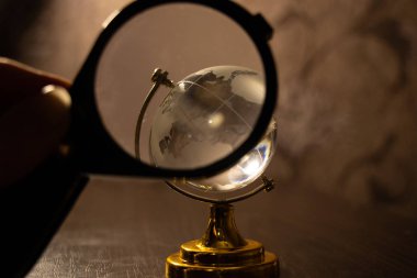 Bir büyüteç, karanlık bir odada masanın üzerinde duran şeffaf bir cam küreye nişan alınır.